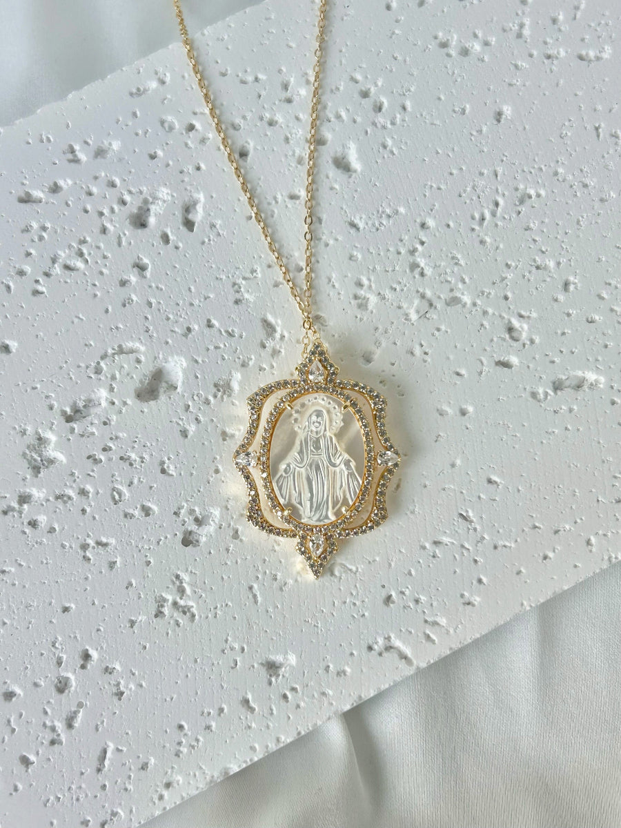 Gold necklace with a religious pendant on a textured white surface